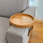 Tablette d'accoudoir ronde NESTIVA en bois naturel installée sur l'accoudoir d'un canapé gris
