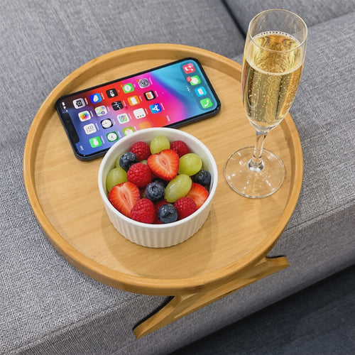Vidéo : tablette d'accoudoir NESTIVA en bois sur un canapé gris, avec un verre, un téléphone et des fruits